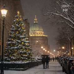 two people walking down a snowy street in front of a christmas tree with lights on it