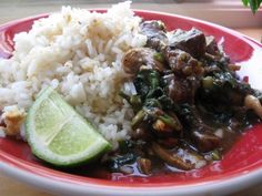 a red plate topped with rice and meat covered in gravy next to a slice of lime