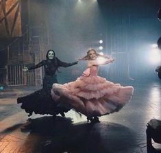 two women in long dresses are dancing on the dancefloor with lights behind them