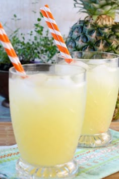 two glasses filled with lemonade sitting on top of a table next to pineapples