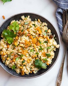 a bowl filled with rice and vegetables on top of a white table next to silverware