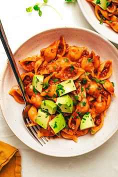 two bowls filled with pasta and vegetables on top of a white table cloth next to a fork