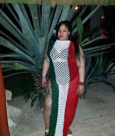 a woman standing in front of a palm tree wearing a red, white and green dress