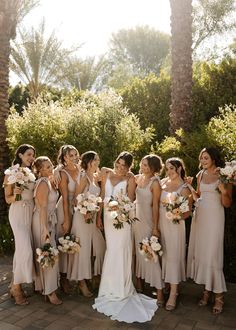 a group of women standing next to each other in front of some trees and bushes