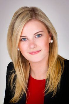 a woman with blonde hair and blue eyes wearing a black blazer, red shirt and pearl earrings