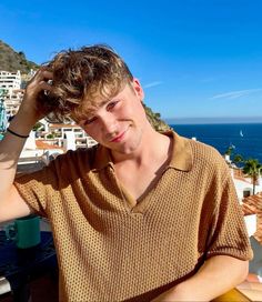 a young man sitting on top of a roof next to the ocean with his hands in his hair