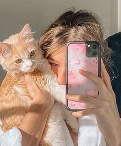 a woman holding a cat and taking a selfie with her phone