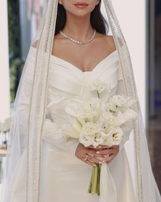 a woman in a white wedding dress holding a bouquet of flowers and wearing a veil