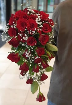 a man holding a bouquet of red roses in his hand while standing on a tiled floor