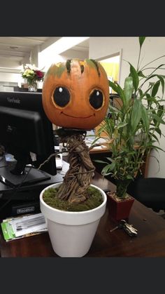 a pumpkin head sitting on top of a potted plant next to a computer monitor