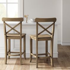 two wooden chairs sitting next to each other on top of a hard wood floor in front of a window