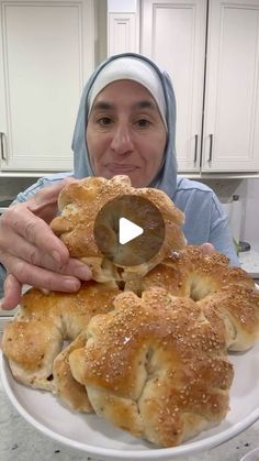 a woman in a headscarf is holding up some bread rolls on a white plate