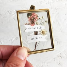 a hand holding up a tiny photo frame with flowers on it that says grow old with me