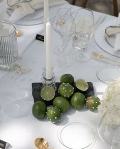 limes and white flowers on a table with silverware, candles and napkins