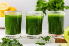 three glasses filled with green liquid next to sliced apples