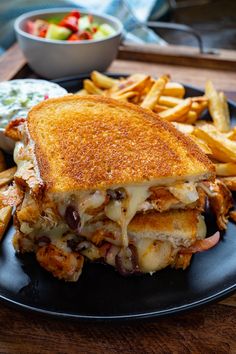 a grilled cheese sandwich and french fries on a black plate with a bowl of salad in the background