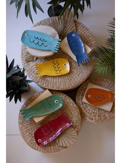 three decorative fish on wicker plates next to potted plant