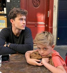 a young man sitting next to a little boy at a table with a cell phone