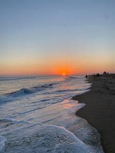 the sun is setting over the ocean with people on the beach and in the water