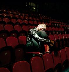 a woman sitting in the middle of a row of red chairs with her head down