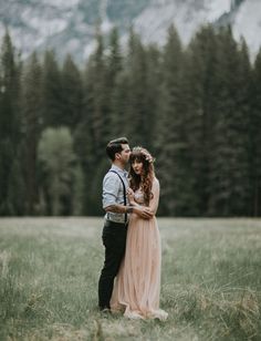 a man and woman standing in a field with mountains in the backgrouds