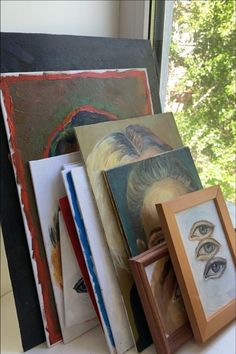 an assortment of art work displayed on a window sill with trees in the background