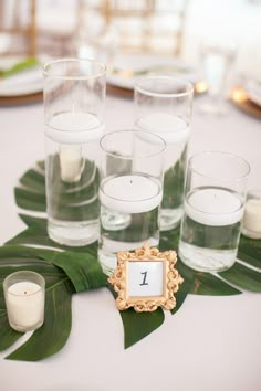 a table topped with lots of glasses filled with water and candles next to each other