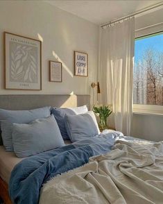 a bed with blue sheets and pillows in a bedroom next to a window that looks out onto the trees