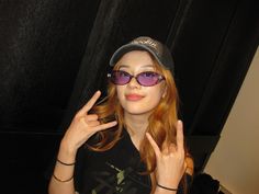 a woman wearing sunglasses and a hat making the peace sign