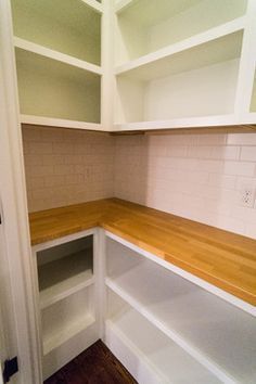 an empty pantry with white cabinets and wood counter tops, in the corner of a room