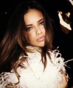 a woman with long hair wearing a white feathered jacket and posing for the camera