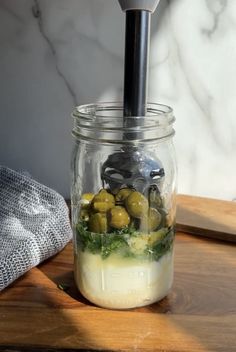 a glass jar filled with olives and cheese on top of a wooden cutting board