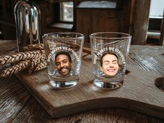 two shot glasses with faces on them sitting on a wooden tray