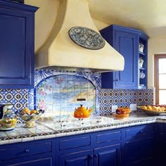 a kitchen with blue cabinets and tile backsplashes on the counter top, along with bowls of fruit