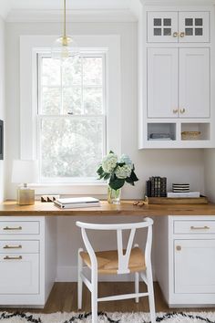 a white desk and chair in a small room with wooden floors, windows, and cabinets