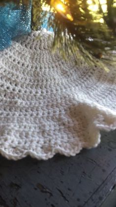 a crocheted table cloth sitting on top of a wooden table next to a pine tree