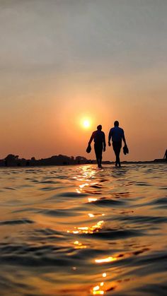 two people walking into the ocean at sunset