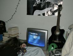 a woman laying in bed next to a tv and guitar