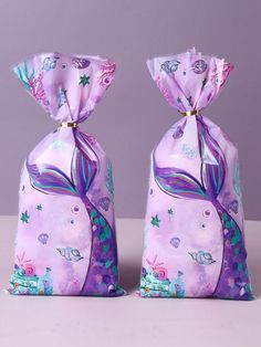 two purple bags with mermaid designs on them sitting next to each other in front of a gray background