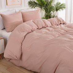 a bed with pink comforters and pillows in a room next to a potted plant