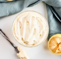 a bowl of whipped cream next to sliced oranges and a spoon on a white surface