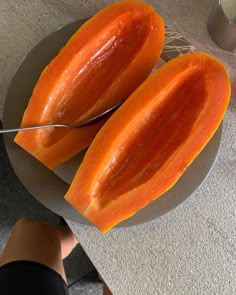 two pieces of papaya are on a plate with a knife next to it and someone's leg in the background