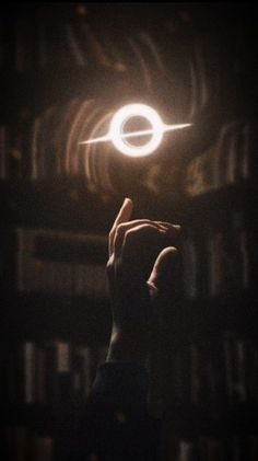 a person holding their hand up in the air with a glowing object above them and bookshelves behind