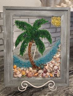 a glass painting of a palm tree and sea shells in a frame on a table