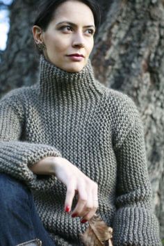 a woman wearing a turtle neck sweater in front of a tree with her hand on her hip