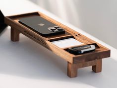 two cell phones are sitting in a wooden tray on a white table top with a black bag next to it