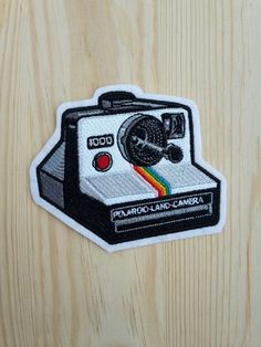 a polaroid camera embroidered patch on a wooden surface