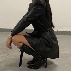 a woman sitting on top of a chair in a black dress and high heeled boots