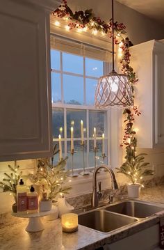 a kitchen sink under a window with christmas lights hanging from it's side and candles on the windowsill