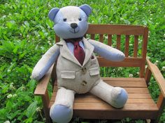 a teddy bear wearing a suit sitting on a bench in the grass with flowers behind it